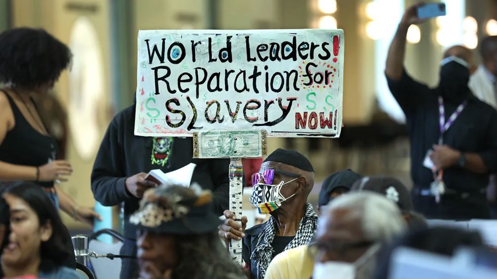A man holds up a sign during a public hearing on reparations at the California Science Center in Los Angeles, CA on September 22, 2022.