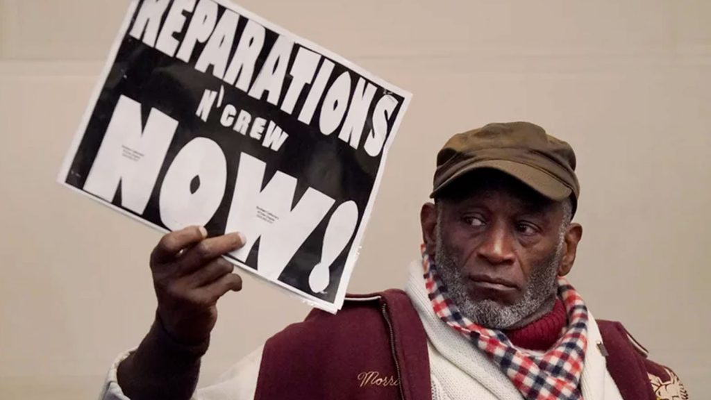 Globally, attitudes toward reparations are changing, experts say. Morris Griffin (pictured) holds up a sign during a meeting by the Task Force to Study and Develop Reparation Proposals for African Americans in Oakland, Calif.