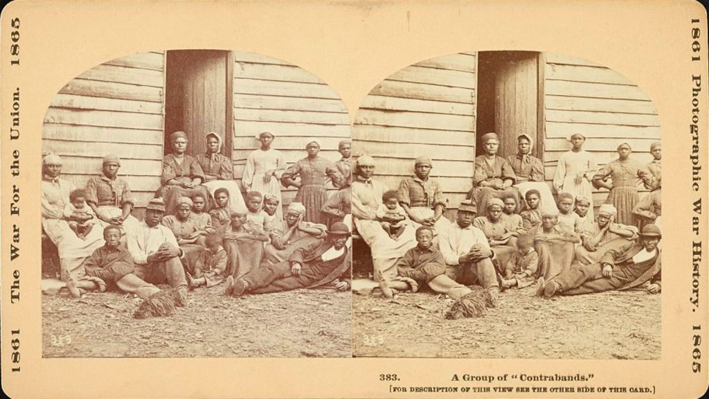 Stereograph showing a group of escaped slaves including men, women, and children gathered outside a building at the Foller Plantation in Cumberland Landing, Pamunkey Run, Virginia. May 14, 1862.