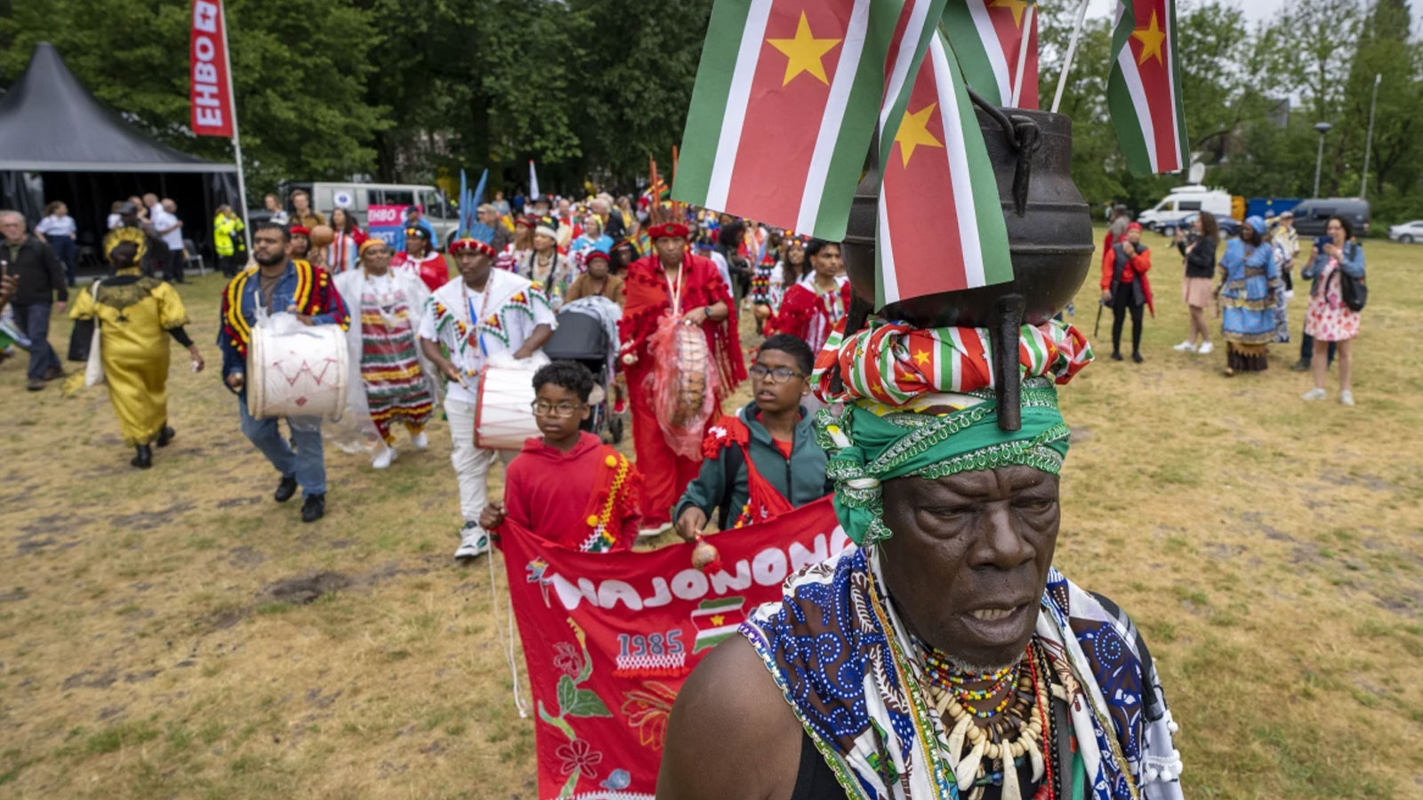 The flags of Surinam, a former Dutch colony, sit in a kettle atop the head of a man leading a procession of people attending the ceremony where Dutch King Willem-Alexander is to deliver a speech in Amsterdam, Netherlands, Saturday, July 1, 2023, at the start of a year to commemorate the 150th anniversary of abolition by the Netherlands of slavery. The king’s speech follows Dutch Prime Minister Mark Rutte saying sorry late last year for the country’s role in the slave trade and slavery.