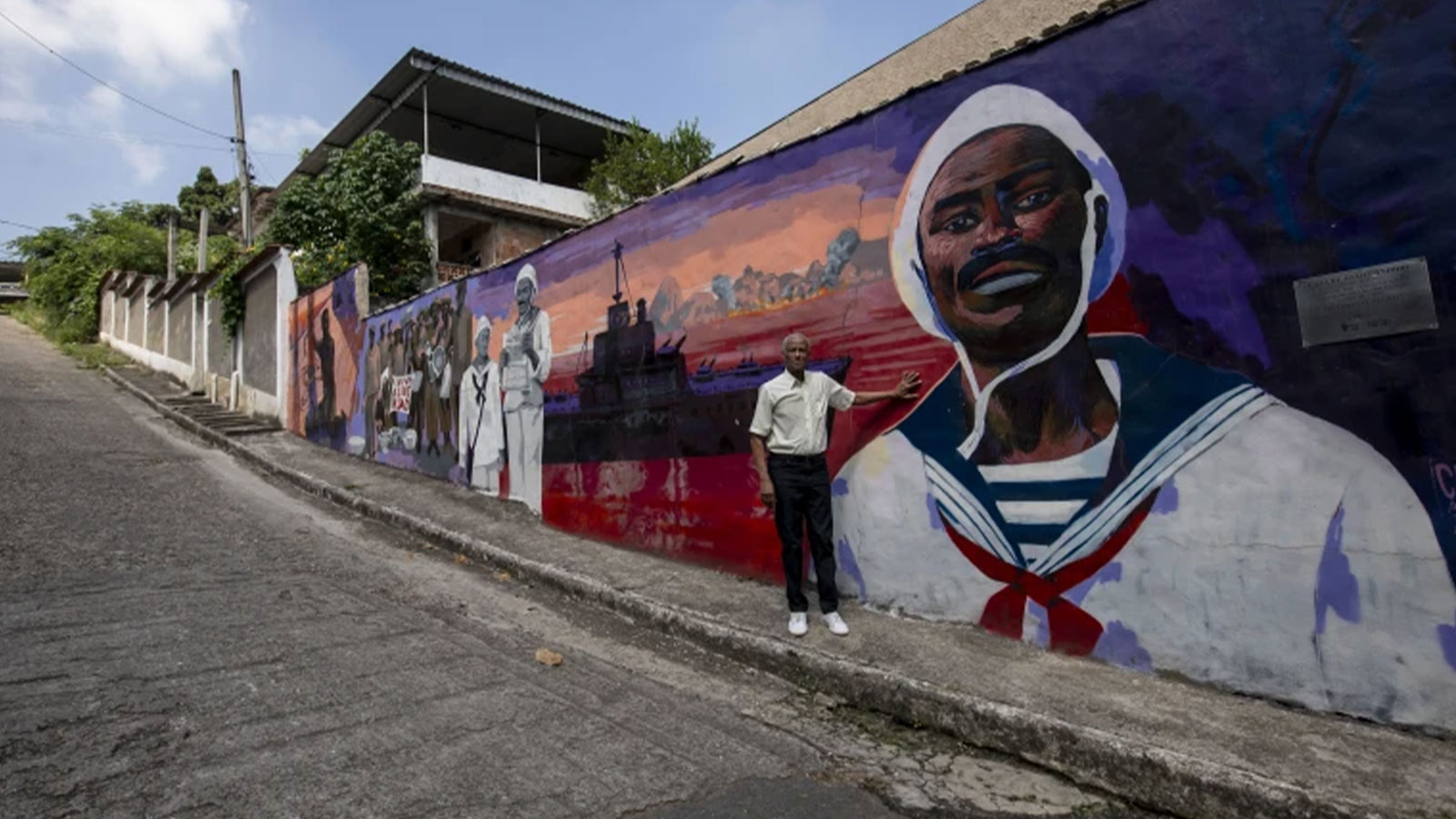 Adalberto Cândido poses for a photo in front of a mural that depicts the story of his father João Cândido, a black sailor who led a revolt against the Brazilian Navy, in Sao Joao de Meriti, Rio de Janeiro state, Brazil, Thursday, Dec. 21, 2023.